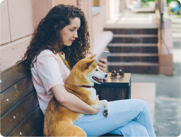 girl with brown hair browsing her phone while holding dog